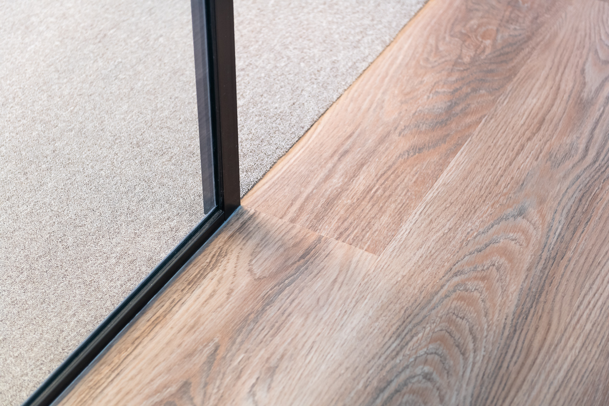 overgang tapijttegels naar pvc vloer met eikenlook met daarop glazen systeemwand met zwarte profilering